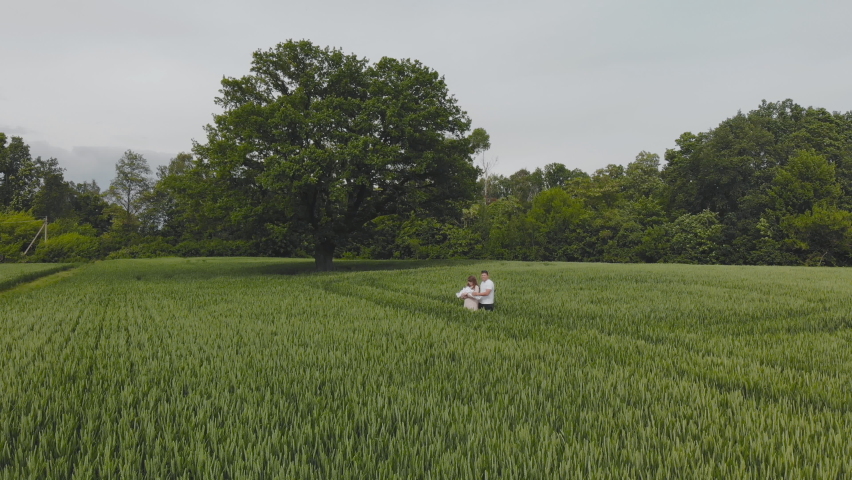 A young couple with their newborn baby in green wheat in a field.