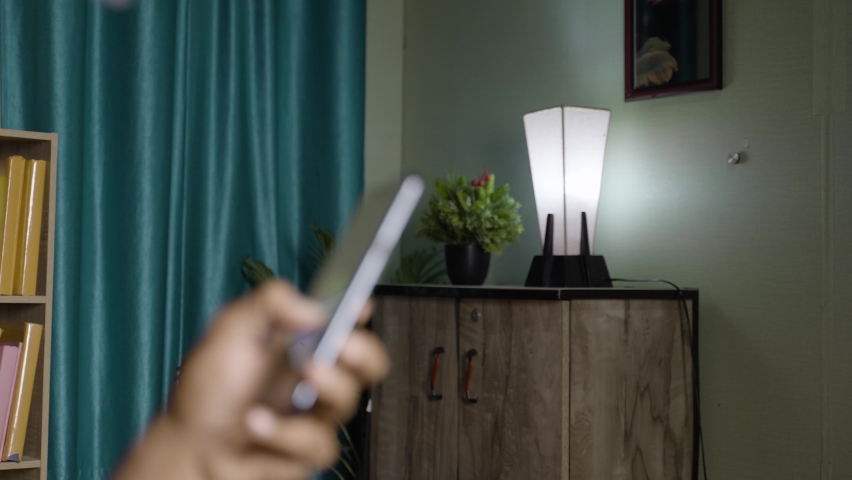 Focus on lamp, close up shot unrecognizable person controling smart bulb using mobile phone at home - concept of technology, IOT devices, | Shutterstock HD Video #1085487971