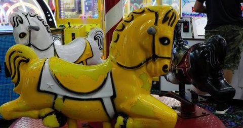 Old worn out and distressed kids yellow and white merry go round toy ride sits with new arcade games with flashing lights being used around it - in Cinema 4k (30fps slowed from 60fps).