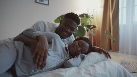 Tender moments. Zoom in portrait of young african american pregnant lady wearing pajamas resting on bed with her husband, stroking big belly together at home, slow motion