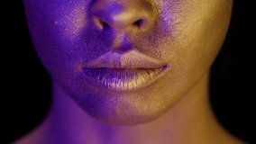 Closeup Of Female Lips, Mouth And Lower Part Of Face With Golden Skin Over Black Studio Background In Neon Light. Cropped Portrait Of Woman Covered With Gold Facial Paint. Beauty And Fashion Art