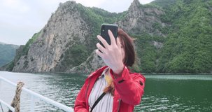 Happy woman making travel stories on phone. Ferry on turquoise mountains lake. Traveler talking on video call while traveling on ship board. Making video for social media. Adventure, explore world