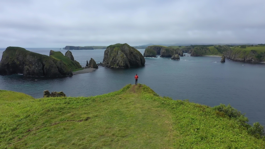Drone Flying Over Traveler on a Cliff in Beautiful Unnamed Bay, Shikotan Island, Lesser Kuril Chain, Coastline of Pacific Ocean, Russia. Royalty-Free Stock Footage #1085502584
