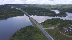 From a bird 's - eye view . Clip. A large green forest with a bridge on which cars drive passing through the river with a cloudless sky in the background.
