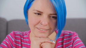 Happy white woman with dyed blue hair reading from computer screen in 4k footage. Beautiful focused female with cheerful smile filmed in closeup stock video
