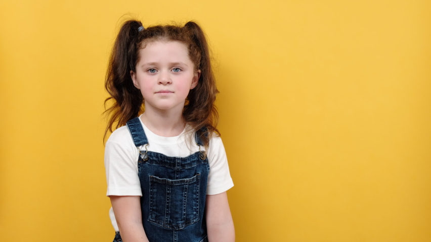 Portrait of smiling cute little girl kid holding white paper key model, isolated on yellow color background wall in studio with copy space. Real estate, insurance concept, mortgage, realtor concept