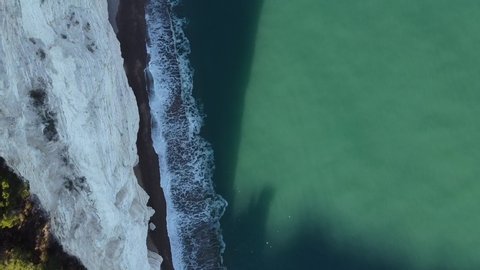 The drone flies over the top of the rock face. View from above of the vegetation on top of the cliff and of the sea waves crashing on its slopes