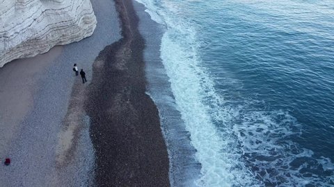 The drone films an engaged couple strolling on the white beach by the sea on the slopes of the cliff. Romantic walk full of love and hugs on Valentine's Day