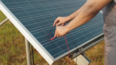 Close up of male hands checking voltage in solar panels with multimeter outdoors. Competente energy technician controlling work of solar station. Man checking voltage in solar panels with multimeter.