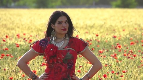 Gypsy girl in a field of poppies in slow motion. Red gypsy dress. Beautiful brunette woman in nature.