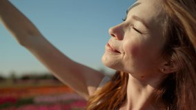 Portrait of beautiful woman looking at sun. Closeup young woman closing eyes on bright sun outside. Smiling girl wrinkling on sun in summer day outdoors. Pretty girl raising hand to sunlight outdoor.