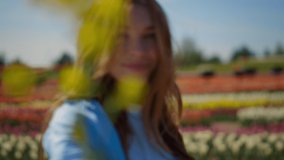 Portrait of smiling woman dancing in flower field outdoors. Flirty girl with long red hair turning around in spring park. Closeup young female person feeling free in blooming garden in summer day.