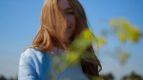 Playful girl with wild hair showing rape branch in summer day. Smiling woman playing with wild flower outdoors. Happy female person giving green plant in blue sky background. Jolly girl smelling colza - Powered by Shutterstock - Get 15% off with code: PIKWIZARD15