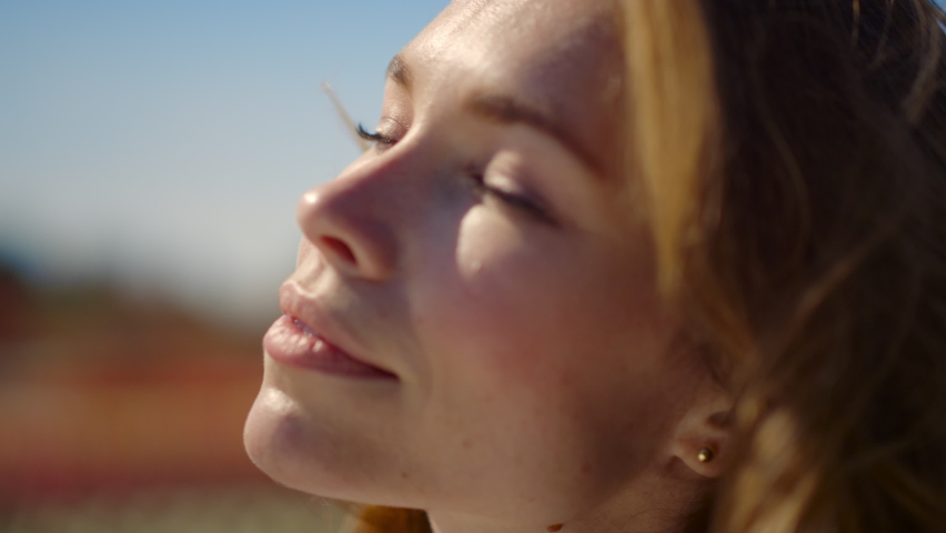 Closeup beautiful woman face enjoying sunshine in nature outdoors. Pretty red hair girl with closed eyes dreaming with smile in summer day outside. Happy female sitting in pleasure in sunlight. 