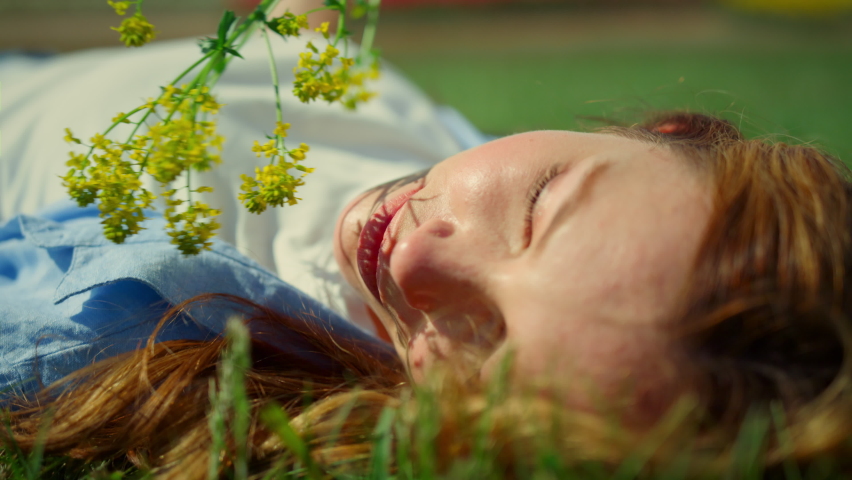 Relaxed girl posing with wild flower in green spring park outdoor. Young woman with branch shadow on beautiful face. Girl with red hair on green grass background. Female person enjoying sun in park.  Royalty-Free Stock Footage #1085515607