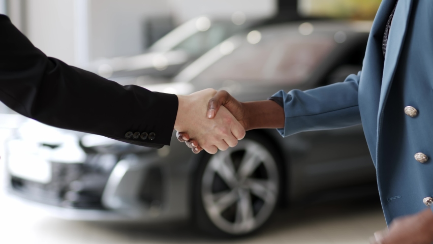 Car salesman finishing up dealing electric car and shaking hands. Businessman giving car key to a african american black woman in automotive dealership showroom 4K | Shutterstock HD Video #1085517299