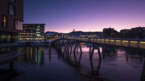 Beautiful Sunrise over The Flower Bridge in Trondheim, Norway. People crossing the bridge while purple and blue colors appear in the sky. Timelapse.
