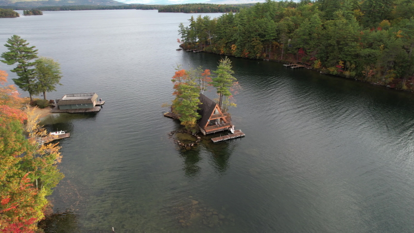 Lake lodge on island. Aerial view of house on islet in colorful autumn landscape of Winnipesaukee lake, New Hampshire USA, orbiting drone shot