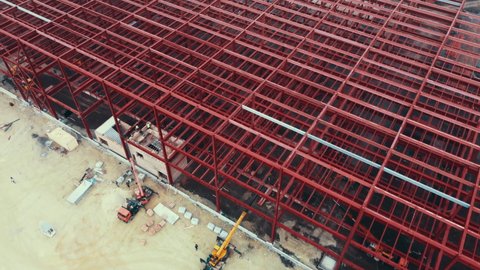 Construction of warehouse from metal structures. Industrial building on light gauge steel framing. Frame of modern hangar or factory. Aerial view of a construction site with steel structure warehouse