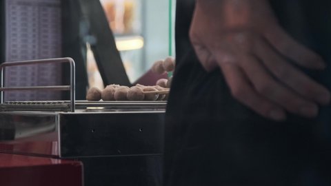 Hand of a merchant toasting meatballs on skewers on an electric stove. Street food in Thailand.