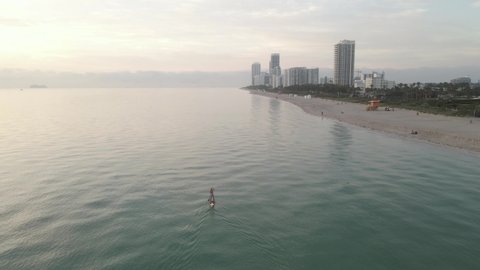 Aerial overtakes lone paddleboarder off sand beach as Miami wakes up