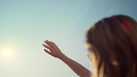Back view of young woman with photocamera looking at hand on sunshine background outdoors. Religious concept. Young modern woman looking at sunbeam through fingers. Closeup sunlight through woman hand