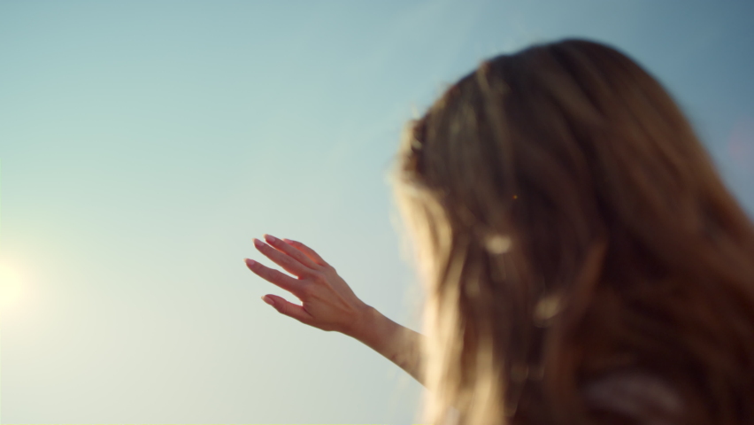 Back view woman with beautiful hair staying against sun. Girl holding hand in sunlight. Religious concept. Closeup woman playing sunbeam with fingers outdoors. Female standing in front of sunshine. 