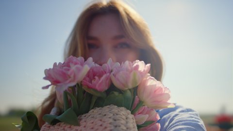 Portrait of beautiful woman smelling gentle pink flowers in sun reflection. Closeup smiling lady face with fresh spring flower bouquet in sunlight. Face of blue-eyed happy girl enjoying flower buds.