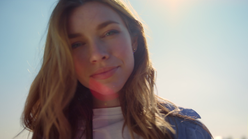 Portrait of beautiful woman in sunlight. Smiling woman face in blue sky background and sunbeams. Portrait of gentle female person looking at camera with love. Blue-eyed girl posing in sunshine outdoor Royalty-Free Stock Footage #1085534444