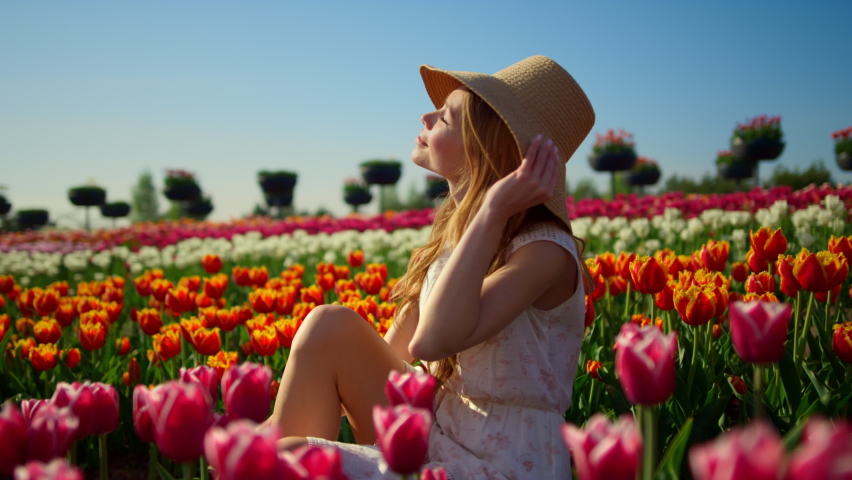 Fancy woman enjoying sun in beautiful holland tulip field. Cheerful woman taking off sunhat in summer sunny day. Relaxed girl turning face to sun in spring flower garden. Girl in blooming spring park. Royalty-Free Stock Footage #1085534489