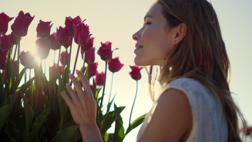 Closeup woman profile smelling spring flower in blooming garden outdoors. Smiling girl enjoying tulips in sun reflection bright sunny day. Close up beautiful female touching floral bud in sun beams. Royalty-Free Stock Footage #1085534534