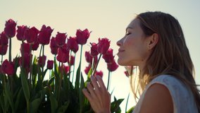 Closeup woman profile smelling spring flower in blooming garden outdoors. Smiling girl enjoying tulips in sun reflection bright sunny day. Close up beautiful female touching floral bud in sun beams. - Powered by Shutterstock - Get 15% off with code: PIKWIZARD15