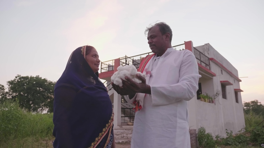 A middle-aged traditional male farmer with a wife is standing in front of the house holding some raw or unprocessed cotton in his hands. Concept of Agriculture, rural family or couple and textile