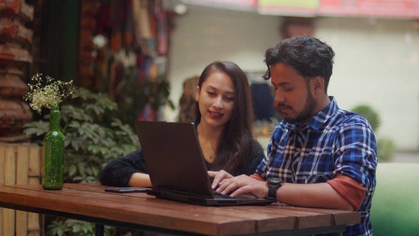 cheerful modern young male and attractive female sitting together in an outdoor sidewalk cafe and restaurant having a conversation and smiling together while looking at the screen of a laptop Royalty-Free Stock Footage #1085534666