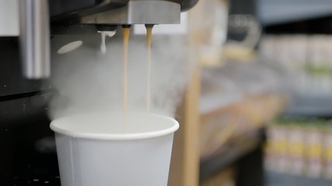 Two streams of hot cappuccino are poured into a paper cup in a coffee machine. Aromatic coffee to go for a walk in the open air