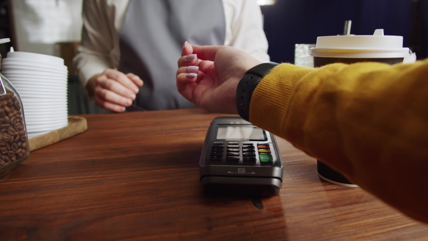 Paying with smartwatch in cafe. Contactless, touch-free shopping in pubs. NFC technology concept, using fitness bracelet payment via terminal close-up.  Royalty-Free Stock Footage #1085547848