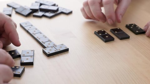 Couple playing dominoes at home. Caucasian husband and wife with Parkinson's disease play dominoes. Close-up of hands.