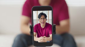 Headshot asia people mature young adult male vlogger with good luck red shirt happy laugh smile look at camera in dating call film smartphone app. Influencer live stream on vlog webcam at home sofa.