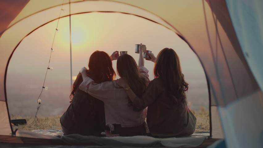 Friendship group of Asian young women having fun and enjoy Sit together, cuddle, drinking coffee, and watch the sunset. outdoor camping trip in nature, Females Lifestyle Vacations Relaxation.