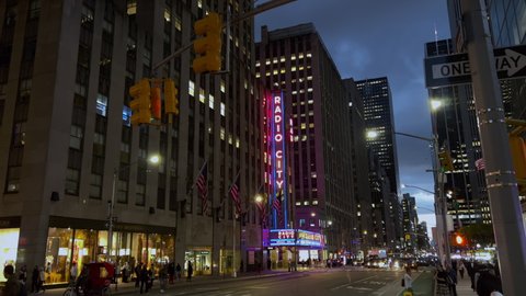 NEW YORK, USA - OCTOBER, 24, 2021: Radio City Hall. 6th avenue street in the NYC city at night. Road, people, traffic, intersection. Buildings in midtown Manhattan, traffic lights.