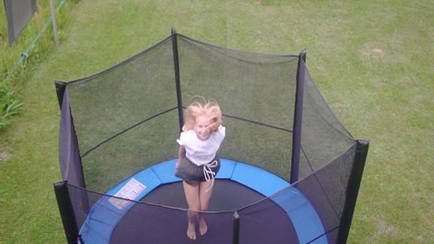Red-haired teen girl jumps on a trampoline. Girl having fun while relaxing in a country house.