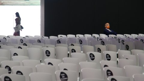 Bologna, Italy, 17 Gen 2022 - conference center in Bologna with empty chairs for social distancing seats during the Covid-19 pandemic with masked man and people on background