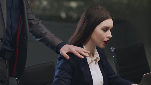No to sexual harassment. Lustful man boss touching his young attractive female assistant at office, unhappy woman rejecting molestation, sitting alone at workplace, tracking shot, slow motion