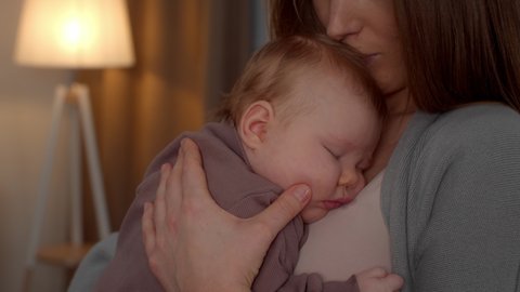 Loving Mother Kissing Adorable Newborn Baby Sleeping On Her Chest, Unrecognizable Young Mom Holding Cute Napping Infant Child, Enjoying Spending Time Together At Home, Slow Motion Footage
