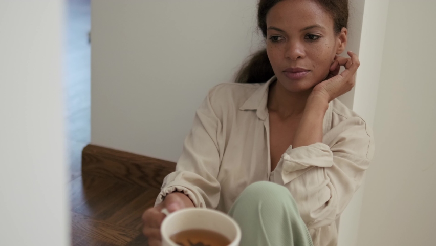 Pensive African woman holding a cup of tea at home