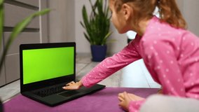 Little girl watching online video on laptop and doing stretching, fitness exercises at home. Child distant training with personal trainer, online education concept, Playing sports, Healthy lifestyle.