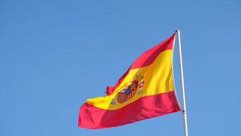 Spanish national flag waving on blue sky background. The flag on a flagpole flutters in the wind. Red with yellow Spain Flag blowing in the wind against on blue sky