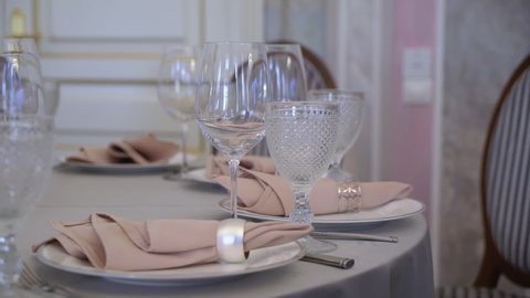 Served table in a restaurant for dinner, lunch or celebration. White tablecloth, plates, pink napkins and glasses, chairs. Holiday indoors. Empty with no people and food. Decorated for wedding.