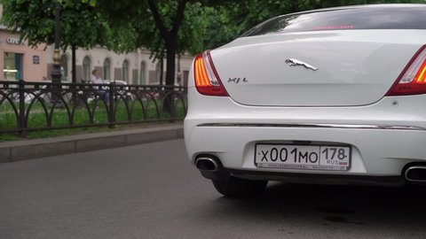 SAINT-PETERSBURG, RUSSIA - JULY, 20, 2021: White luxury sedan Jaguar XJ long car driving in a city street road. Auto vehicle limousine for VIP transportation. Wheel and logo. Rear part of automobile.