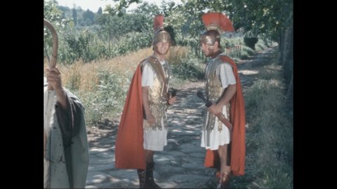 1960s: Men in Roman period costume talking on road. Clapboard. Close up of book, hand points to text.